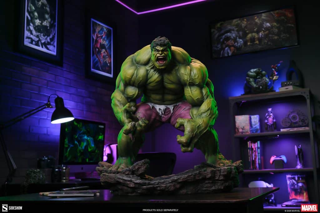 A detailed statue of the Hulk, showcasing his muscular physique and intense expression, placed on a decorative base in a colorful, dimly lit room with gaming accessories and artwork in the background.