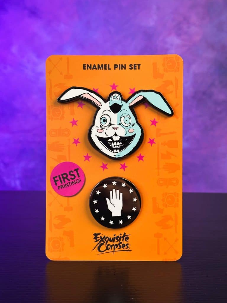 Enamel pin set featuring a cartoonish rabbit with a wide smile and a black and white pin of a raised hand, displayed on an orange card with a pink 'FIRST PRINTING!' sticker.