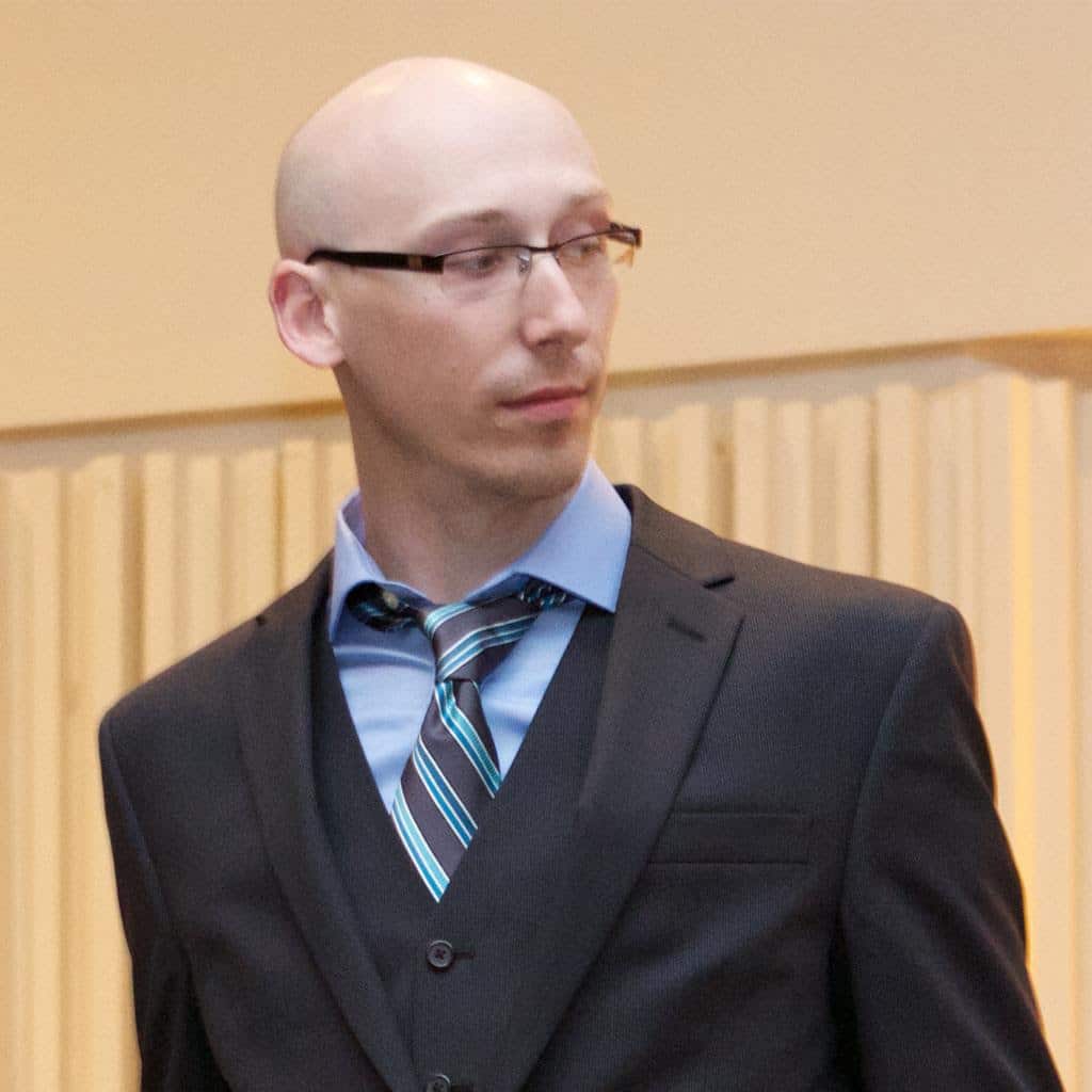 Man in a suit with a vest and tie, looking away from the camera in a formal setting.