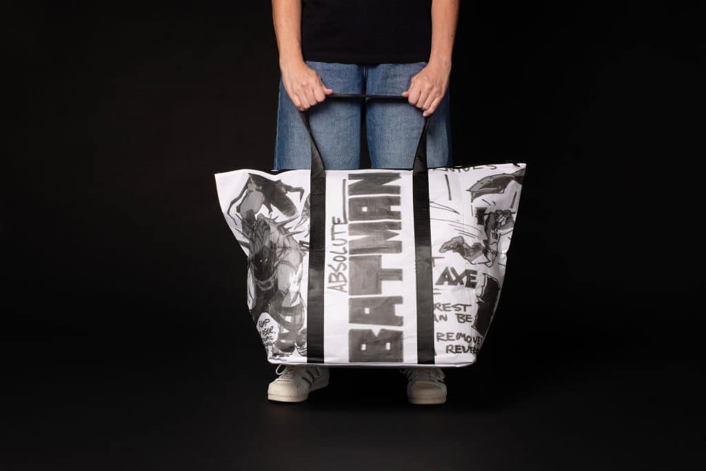 A person holding a large tote bag featuring black and white artwork of Batman, with the word 'ABSOLUTE' prominently displayed.