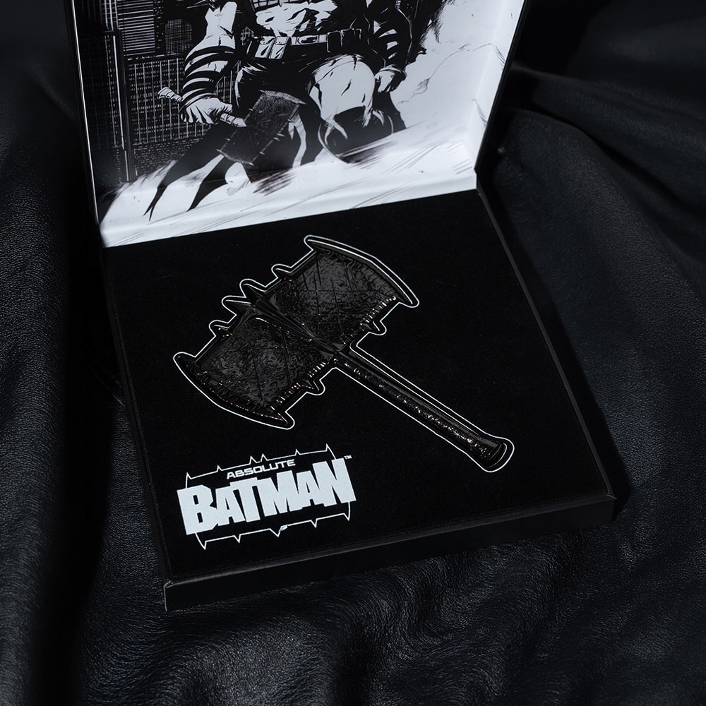 A close-up of a black cardboard display featuring a detailed graphic of a bat-themed axe, with the text 'ABSOLUTE BATMAN' prominently displayed below.