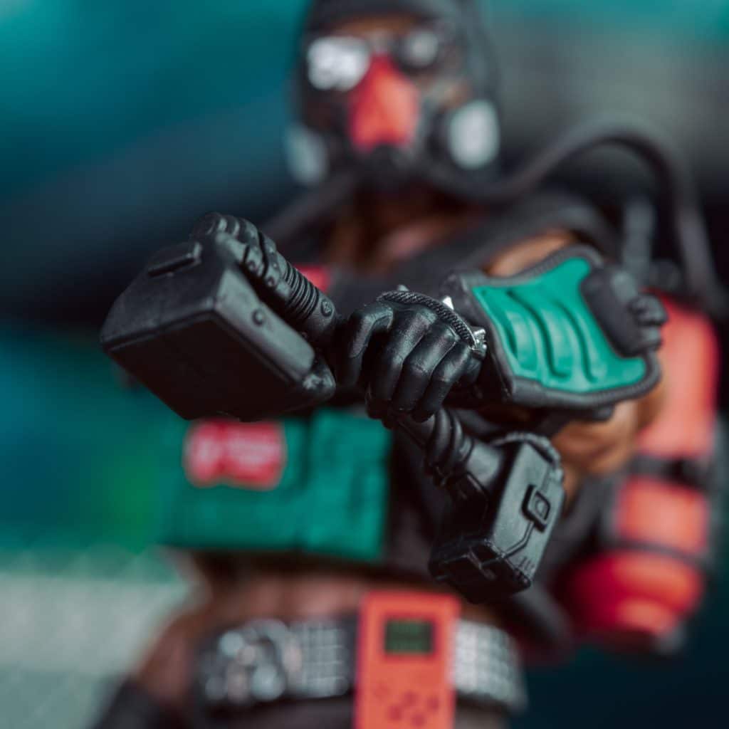 Close-up of a detailed action figure holding a high-tech gadget, wearing a mask and tactical gear, with a blurred background.