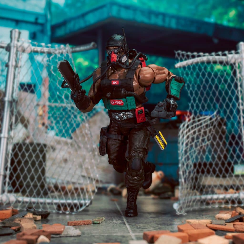 A muscular action figure in tactical gear, equipped with a chainsaw and other tools, running through a debris-strewn area with a chain-link fence in the background.