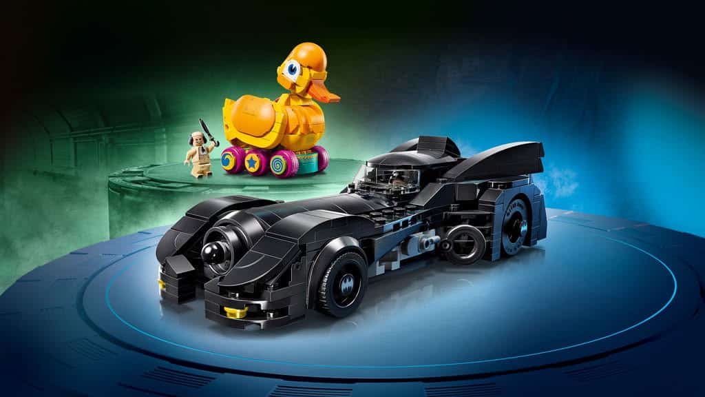 A black LEGO Batmobile in a dynamic pose, with a colorful toy duck on wheels and a small character figure nearby, set against a gradient background.