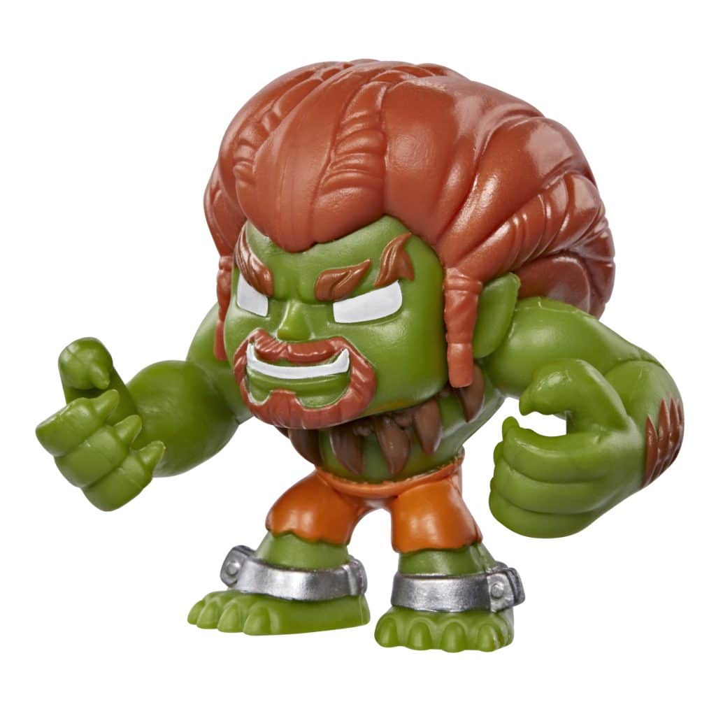 A small green action figure with exaggerated muscular features, wearing orange shorts and silver cuffs, with distinctive red hair styled in a tall, spiky manner.