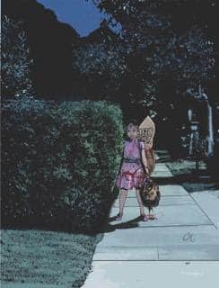A young child wearing a pink outfit stands on a sidewalk beside a bush at night, holding a large toy and looking towards the camera.